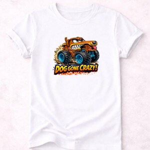 以下が含まれることがあります： 白いTシャツ。犬をモチーフにしたカートゥーンのモンスタートラックのデザイン。トラックは茶色とオレンジ色で、青い車輪があり、「DOG GONE CRAZY!」の文字がカラフルなフォントで表示されています。犬はしかめっ面をしています。
