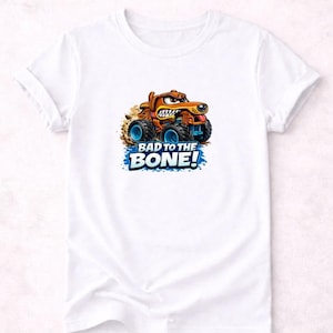 以下が含まれることがあります： 白いTシャツ。モンスターカーに乗った漫画の犬が描かれています。犬は茶色で怒った表情をしており、トラックは青い車輪をしています。「BAD TO THE BONE!」の文字が下に青と白で印刷されています。