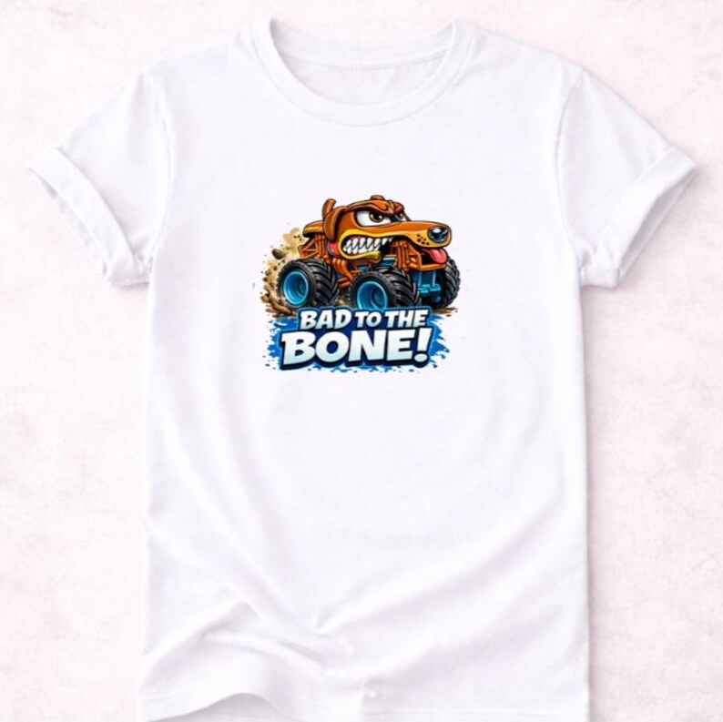 以下が含まれることがあります： 白いTシャツ。モンスターカーに乗った漫画の犬が描かれています。犬は茶色で怒った表情をしており、トラックは青い車輪をしています。「BAD TO THE BONE!」の文字が下に青と白で印刷されています。