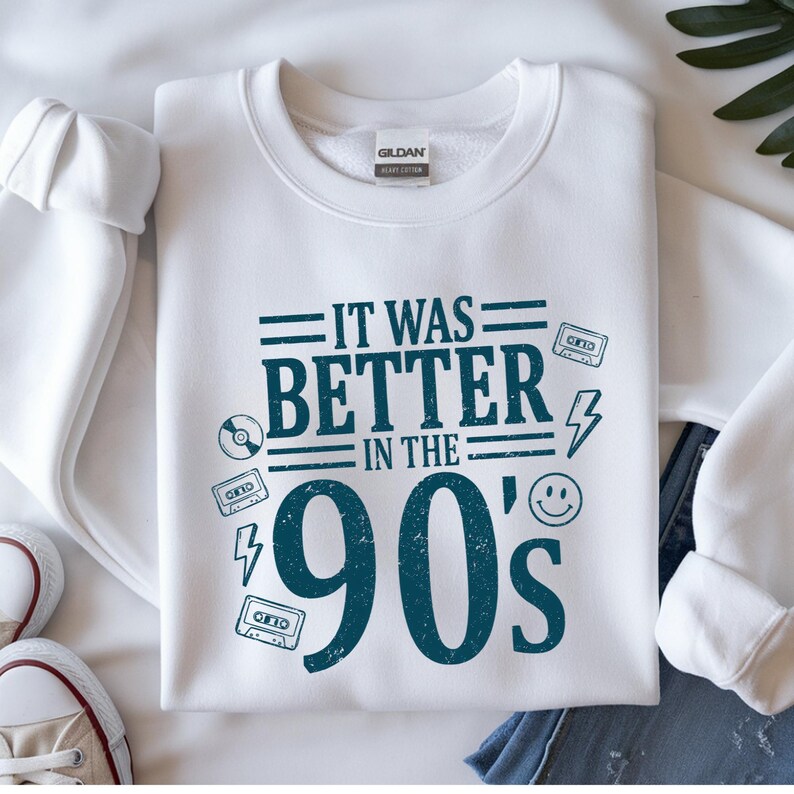 May include: A white crewneck sweatshirt featuring dark teal text that reads IT WAS BETTER IN THE 90's. The design includes graphic elements such as cassette tapes, a lightning bolt, a smiley face, and a compact disc, all printed in a distressed style.