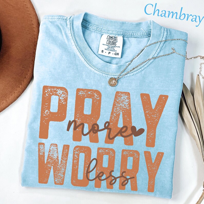 K&ouml;nnte beinhalten: Ein hellblaues Kurzarm-T-Shirt mit verwaschener Optik. Das Shirt tr&auml;gt den Schriftzug PRAY more WORRY less in einer kr&auml;ftigen, rostorangen Farbe. Ein Etikett der Marke Comfort Colors ist am Innenkragen sichtbar und zeigt die Gr&ouml;&szlig;e S an.