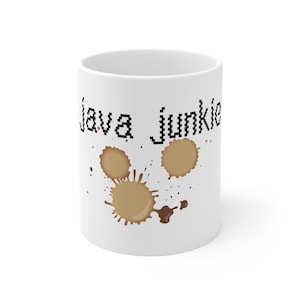 Puede incluir: Taza de café de cerámica blanca con el texto "Java Junkie" en fuente negra pixelada. La taza presenta diseños de manchas de café marrones. Un gran regalo para los amantes del café.