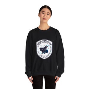 May include: Black sweatshirt featuring a circular graphic with a space shuttle, planets, and the text "CRITICAL SYSTEMS CREW" and "WE RUN THE CHECKLISTS". The design is in white, blue, and black.