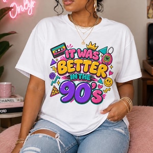 May include: A white short-sleeve t-shirt featuring a colorful graphic print with the text "IT WAS BETTER IN THE 90'S". The design includes illustrations of a cassette tape, a digital pet, a crown, a smiley face, and geometric shapes in bright colors.