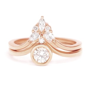 May include: A rose gold engagement ring set with a bezel-set round diamond and a delicate marquise diamond cluster.