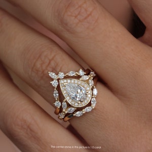 Pear diamond three-ring set, the center stone is a 1.0-carat pear natural diamond or lab diamond. the engagement ring has a diamond halo and marquise diamonds on the band. The engagement ring has two nesting crown chevron wedding rings. solid gold
