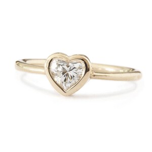 Könnte beinhalten: Ein goldener Ring mit einer herzförmigen Fassung, in der ein klarer Diamant sitzt.