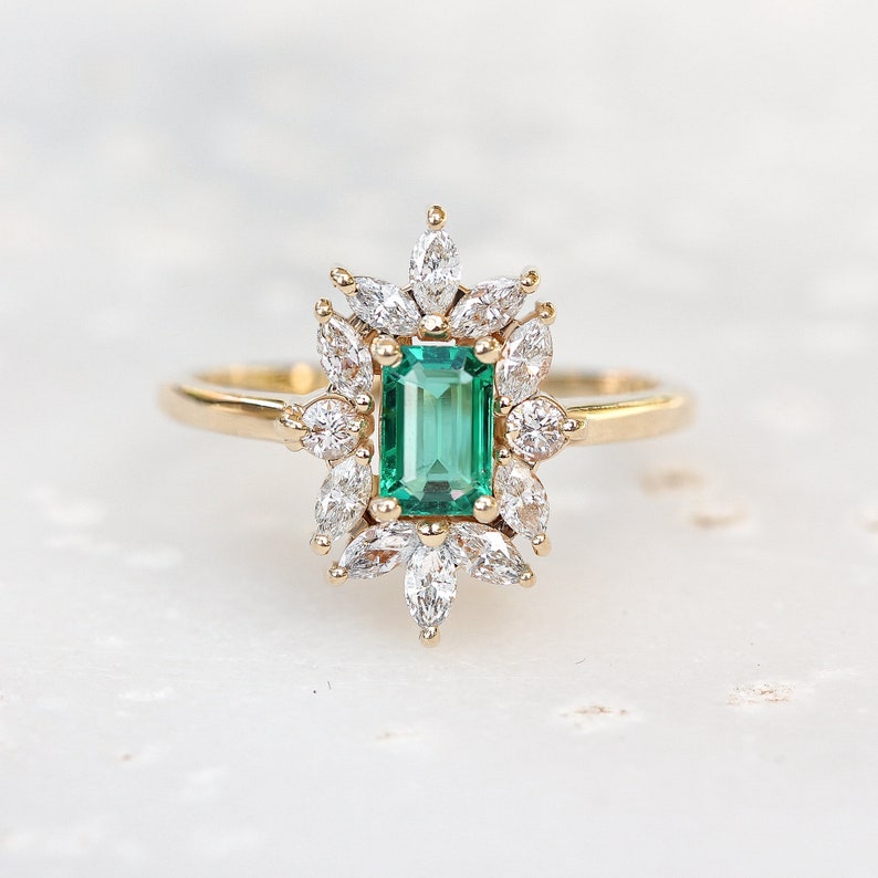 May include: A gold ring with a large emerald green gemstone surrounded by smaller diamonds in a floral design.