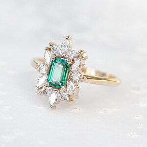 May include: A gold ring with a large emerald green gemstone surrounded by smaller diamonds. The ring has a delicate, floral design.