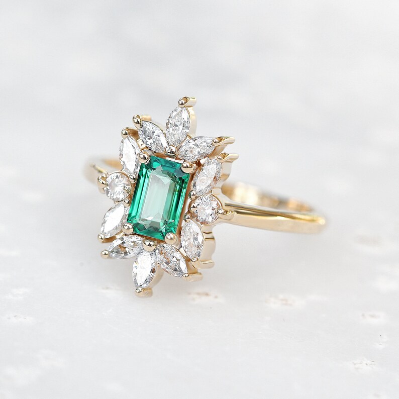 May include: A gold ring with a large emerald green gemstone surrounded by smaller diamonds. The ring has a delicate, floral design.