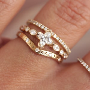 May include: Three gold rings with diamonds. The center ring features a large, four-pointed diamond. The ring on the left has a chevron pattern and the ring on the right has a row of small diamonds.