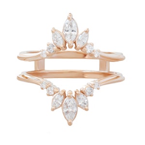 May include: A rose gold ring enhancer with a delicate design featuring marquise-shaped diamonds. The enhancer has a crown-like top and a cascading bottom with smaller round diamonds.