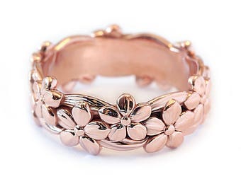 May include: Rose gold ring with a floral pattern. The ring showcases detailed, three-dimensional flowers, giving a delicate and feminine look. The band is smooth and polished, enhancing the floral details. A beautiful piece of jewellery.
