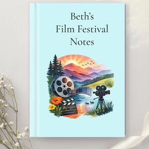 May include: A light blue notebook with the text "Beth's Film Festival Notes" printed in black. The cover features a colorful illustration of a film reel, a clapperboard, a movie camera on a tripod, and a landscape with mountains and a sunset.