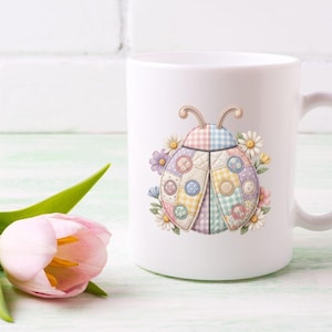 May include: White ceramic mug featuring a colorful ladybug design with a patchwork pattern. The ladybug is surrounded by daisies and other flowers. The mug has a curved handle.