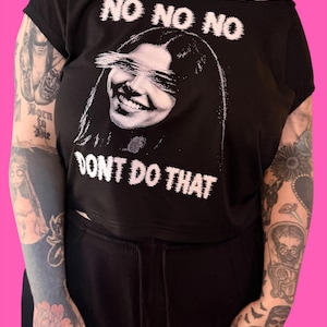 May include: A black short-sleeved t-shirt featuring a white graphic print of a smiling face with eyes obscured by horizontal lines. The text NO NO NO is printed above the face and DONT DO THAT is printed below the face in a distressed font.