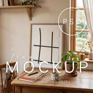 May include: A framed artwork with a black grid design on a cream background sits on a wooden desk. A potted plant, a mug, a notebook, and a pen are also on the desk. The words "frame MOCKUP" and "CREATED BY DUSTANDDARLINGMOCKS" are visible.