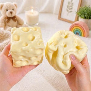 May include: Two yellow, cheese-shaped objects with holes are held in hands. One is a rectangular block, the other is a soft, squishy shape. The objects are a light yellow color and appear to be made of a soft material.
