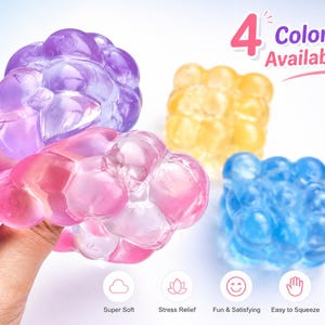 May include: Four colorful bubble-shaped stress balls in purple, pink, yellow, and blue. The pink ball is being held by a hand. Text reads "4 Colors Available!" and icons indicate the balls are super soft, stress-relieving, fun, and easy to squeeze.