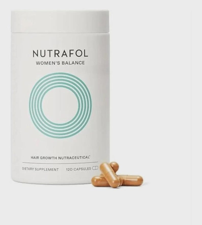 May include: A white cylindrical bottle of Nutrafol Women's Balance hair growth supplement with a teal circular design. The bottle is labeled "Hair Growth Nutraceutical" and "Dietary Supplement, 120 Capsules." Several brown capsules are next to the bottle.