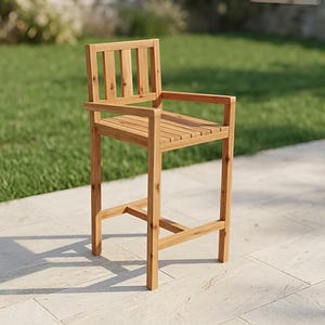 Puede incluir: Taburete de bar de madera con acabado natural. El taburete tiene asiento y respaldo de listones, con reposabrazos. Las patas son robustas y reforzadas. La silla está al aire libre en un patio de piedra, con hierba verde al fondo.