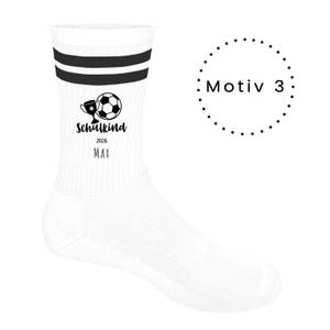 Könnte beinhalten: Eine weiße Socke mit zwei schwarzen horizontalen Streifen am oberen Rand. Das Design zeigt eine schwarze Grafik eines Pokals und eines Fußballs sowie den Text "Schulkind", "2026" und "MAX" in Schwarz, ergänzt durch den Text "Motiv 3".
