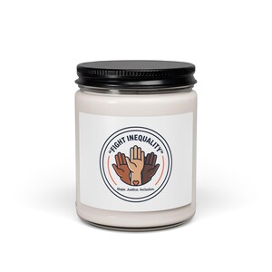 May include: A white jar candle with a black lid. The label features a graphic of hands in different skin tones inside a circle with the words "FIGHT INEQUALITY" and "Hope. Justice. Inclusion."