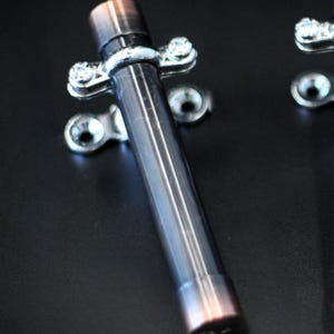 Könnte beinhalten: Drei metallische Türriegel in Kupfer- und Dunkelgrautönen werden vor einem schwarzen Hintergrund gezeigt. Jeder Riegel hat einen zylindrischen Körper und ist mit silberfarbener Hardware montiert. Die Riegel sind für die Sicherheit konzipiert.