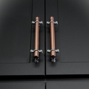 May include: Close-up of four dark gray cabinet doors with copper-colored bar handles. The handles are mounted with silver-colored hardware. The cabinet doors are arranged in a two-by-two grid.