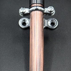 May include: A copper-colored metal door bolt with a cylindrical body and a silver-colored mounting plate. The bolt has a textured finish and is designed for secure door closure. The bolt is made of metal and is likely for home improvement.