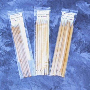 May include: Three packages of hand-crafted birch weaving sticks. Each package contains multiple light-colored wooden sticks with pointed ends. The packages are sealed in clear plastic and labeled with the text "Weaving Sticks" and sizes.