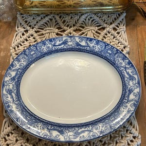 May include: An oval ceramic platter featuring a white center and a wide blue and white border decorated with intricate floral patterns and illustrations of birds. The rim of the platter is accented with a geometric Greek key design pattern.