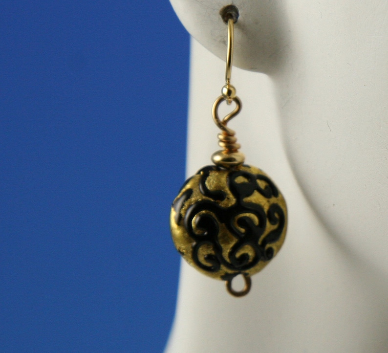 Flame worked lentil shape bead with 23.4 kt gold foil and black stringers in scroll design