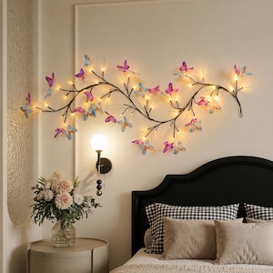 May include: A horizontal wall-mounted light fixture featuring a dark metal branch structure adorned with numerous small, glowing LED lights and translucent, multi-colored butterfly-shaped ornaments in shades of pink, blue, and purple.