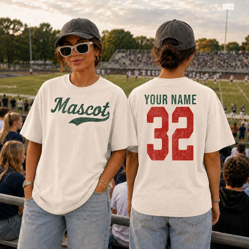 A woman wearing a white t-shirt with the word "Mascot" and the number 32, standing in a stadium with a crowd in the background.