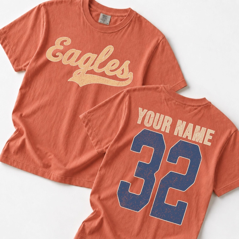Two orange t-shirts with the word "Eagles" printed on them, and one t-shirt with the text "YOUR NAME" and the number "32" printed on it.
