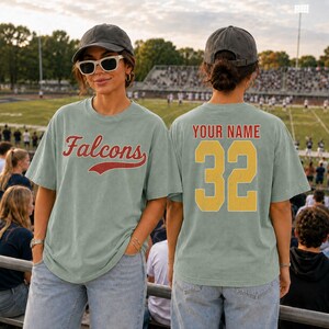 A woman wearing a green t-shirt with the word "Falcons" and the number "32" on it, standing in a stadium with a crowd in the background.