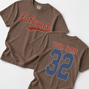 Two brown t-shirts with the word "Falcons" printed on them, and the back of one t-shirt has the text "YOUR NAME" and the number "32" printed on it.