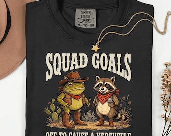 Camiseta con el lema "Causa revuelo, equipo de objetivos" — divertida prenda con estampado de vaquero, rana y mapache.