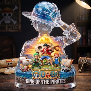 May include: A clear resin display featuring a translucent silhouette of a character wearing a straw hat with a constellation design. Inside, miniature figures of anime characters stand on a base with the text "ODADE" and "KING OF THE PIRATES".