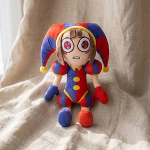 May include: A plush doll in a jester costume with a red, blue, and yellow color scheme. The doll has a large, expressive face with wide eyes and a sad expression. The jester hat is red and blue, and the outfit is a mix of red and blue.
