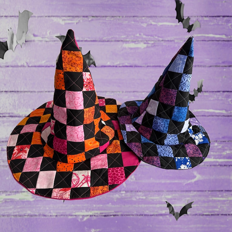 K&ouml;nnte beinhalten: Zwei gesteppte Hexenh&uuml;te mit einem Schachbrettmuster in Orange, Rosa und Schwarz sowie Lila, Blau und Schwarz. Die H&uuml;te haben eine breite Krempe und eine hohe, spitze Krone. Dekorative Flederm&auml;use sind im Hintergrund.