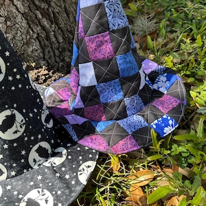 K&ouml;nnte beinhalten: Ein gesteppter Hexenhut mit einem Patchwork-Design in Lila, Blau und Schwarz. Der Hut besteht aus Stoffquadraten, die mit wei&szlig;en N&auml;hten zusammengen&auml;ht sind. Ein zweiter Hut mit einem schwarz-wei&szlig;en Mond- und Sternenmuster ist ebenfalls zu sehen.