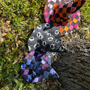 K&ouml;nnte beinhalten: Drei gesteppte Hexenh&uuml;te auf Gras und einem Baumstamm. Ein Hut hat ein schwarz-oranges Schachbrettmuster, ein anderer einen schwarz-wei&szlig;en Totenkopf-Druck, und der dritte hat einen Patchwork aus blauen, lila und schwarzen Quadraten. F&uuml;r Halloween oder Kost&uuml;mpartys.
