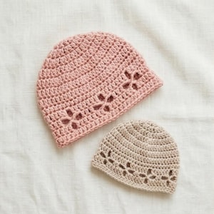 Puede incluir: Dos gorros de ganchillo hechos a mano. Uno es de color rosa suave y el otro de color beige claro. Ambos gorros tienen un diseño floral recortado a lo largo del borde inferior. Los gorros están hechos de un hilo suave y probablemente sean para bebés o niños.
