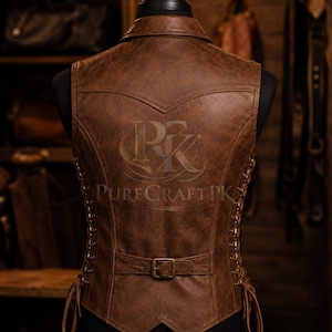 Op de afbeelding: Een bruin leren vest met een distressed afwerking, weergegeven op een mannequin. Het vest heeft een kraag, een gespsluiting in de taille en decoratieve veters aan de zijkanten. De achterkant van het vest heeft een reli&euml;flogo en de tekst "Pure Craft PK".