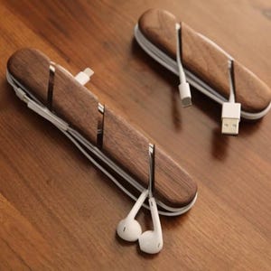 Può includere: Due organizzatori di cavi in legno marrone scuro con cavi e connettori bianchi. Gli organizzatori hanno fessure per tenere i cavi in posizione. Un organizzatore ha auricolari bianchi.