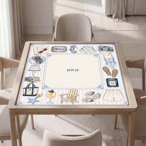 May include: A square table mat featuring a light blue and white striped border with illustrations of a book, sunglasses, seahorse, hat, flowers, swimsuit, sandals, candle, shorts, chair, cocktail, tote bag, and starfish, with the letters RWH in the center.