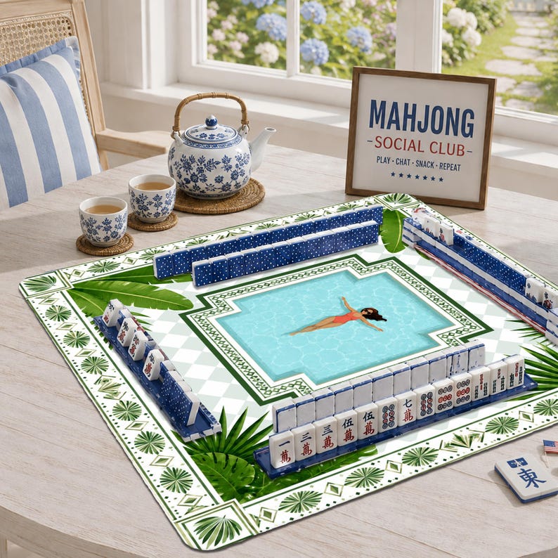 May include: A square mahjong mat featuring a central swimming pool illustration with a person floating, surrounded by green palm leaves and a white diamond pattern. Blue mahjong tiles are arranged in racks, with a teapot and two cups nearby.