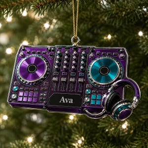May include: A purple DJ controller ornament featuring a central mixer section, two circular platters in purple and teal, and a pair of attached headphones. The name Ava is printed in white text on the centre panel. It hangs from a gold cord.
